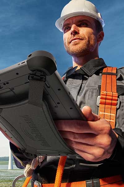 A worker uses a rugged tablet near a wind farm