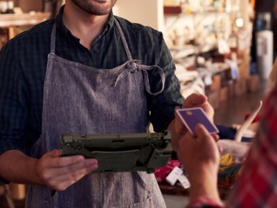 Retail worker holding rugged tablet with integrated payment device taking credit card from customer