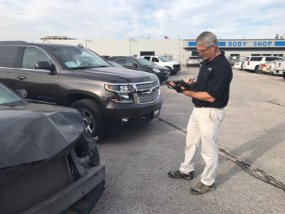 Man taking notes on rugged tablet next to cars