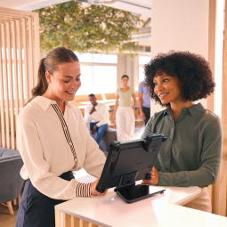 Two women in a hotel lobby using rugged tablet with integrated payment module